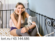 Online dating for single woman 24 years old with help of smartphone, female is sitting on bed in bedroom. Стоковое фото, фотограф Владимир Григорьев / Фотобанк Лори
