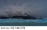 A wall of blue ice with cracks and sharp peaks stretched across the glacial lake. Ripples on the turquoise water. Mountains in clouds and fog. Perito Moreno glacier. El Calafate. Argentina. Стоковое фото, фотограф Вера Ивановна Кубарева / Фотобанк Лори