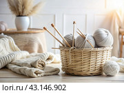 Balls of yarn in a wicker basket in white and beige tones. Needlework, textiles, knitting. Winter season, small business, handmade clothes. Стоковое AI-изображение, AI-художник Photojuli / Фотобанк Лори