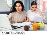 Two women with financial documents near laptop sitting at table at home. Стоковое фото, фотограф Яков Филимонов / Фотобанк Лори