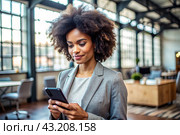 A businesslike dark-skinned African-American woman with curly hair. She is dressed in a casual jacket. In the hands of a smartphone. A businesswoman looks at her mobile phone. Стоковое AI-изображение, AI-художник Photojuli / Фотобанк Лори