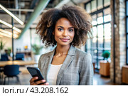 A businesslike dark-skinned African-American woman with curly hair. She is dressed in a casual jacket. In the hands of a smartphone. A businesswoman looks at her mobile phone. Стоковое AI-изображение, AI-художник Photojuli / Фотобанк Лори