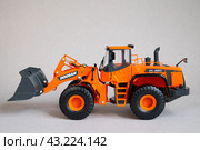 Фронтальный мини-погрузчик Doosan южнокорейского производства для погрузки и транспортировки материалов, земляных работ. Игрушечная миниатюрная модель на сером фоне (2023 год). Редакционное фото, фотограф Дорощенко Элла / Фотобанк Лори