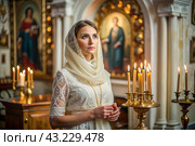 Portrait of a beautiful young woman in a headscarf in an Orthodox church. A girl prays in a church against the background of icons. Стоковое AI-изображение, AI-художник Photojuli / Фотобанк Лори