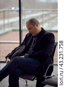 Train Station. Mature man in business clothes is sleeping, sitting in waiting room and waiting for train. Evening is dark. Стоковое фото, фотограф Natalia Gdovskaia / Фотобанк Лори