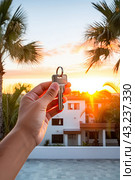 Realtor's hand with keys to house for beach holiday in hot tropics with palm trees. Hotel reservations, booking, moving to new house, mortgage, rent and purchase of real estate. AI generated. Стоковое AI-изображение, AI-художник Ольга Симонова / Фотобанк Лори