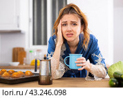 Young woman suffering from migraine, drinking coffee in home kitchen. Стоковое фото, фотограф Татьяна Яцевич / Фотобанк Лори