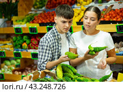 Young family couple chooses fresh bitter melon (Momordica charantia) in grocery supermarket. Стоковое фото, фотограф Яков Филимонов / Фотобанк Лори
