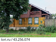 Город Алексин, Тульская область, Россия.  В Старом городе перед современным частным домом стоит необычный забор, представляющий собой переднюю стену старого желтого деревянного дома с окнами (2022 год). Стоковое фото, фотограф Наталья Николаева / Фотобанк Лори