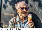 Portrait of an extraordinary, stylish, fashionable elderly woman, a pensioner of 70 years old, with ice cream in her hands on a city street. The concept of happy seniors and delicious desserts. Стоковое AI-изображение, AI-художник Photojuli / Фотобанк Лори