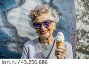 Portrait of an extraordinary, stylish, fashionable elderly woman, a pensioner of 70 years old, with ice cream in her hands on a city street. The concept of happy seniors and delicious desserts. Стоковое AI-изображение, AI-художник Photojuli / Фотобанк Лори