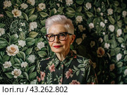 Portrait of a stylish, fashionable elderly woman, a pensioner of 70 years old, wearing glasses and clothes with floral prints. The concept of the elderly. Стоковое AI-изображение, AI-художник Photojuli / Фотобанк Лори