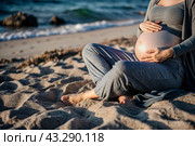 Relaxation, peace of mind, sea air. Close-up of the tummy. A pregnant woman on the beach by the sea. The concept of pregnancy, childbirth and parental responsibilities. Стоковое AI-изображение, AI-художник Photojuli / Фотобанк Лори
