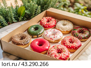 Delicious dessert. A sick box of different donuts with colorful sprinkles on the table. Confectionery products. Стоковое AI-изображение, AI-художник Photojuli / Фотобанк Лори