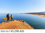 BAIKAL LAKE, OLKHON ISLAND, KHUZHIR VILLAGE, RUSSIA - October 07, 2023: Tourists with backpacks travel around Olkhon Island and admire beautiful view of Saraisky Bay from Burkhan cliff. Редакционное фото, фотограф Виктория Катьянова / Фотобанк Лори