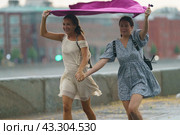 Moscow, Russia - July 10, 2022: Rainy day in the Moscow city at summer. Two young wet pretty  women runs under towel on the city street. Texture of strong, fresh and powerful water drops and sprays. Редакционное фото, фотограф YuryKara / Фотобанк Лори