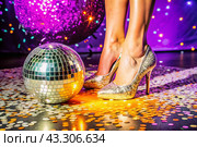 Women's legs in luxurious shiny pumps with heels at a party or disco on the background of a silver mirrored disco ball. The queen of the dance floor. Стоковое AI-изображение, AI-художник Photojuli / Фотобанк Лори