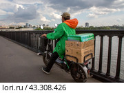Курьер сервиса доставки продуктов Сбермаркет доставляет заказ по Крымскому мосту в центре города Москвы, Россия (2024 год). Редакционное фото, фотограф Николай Винокуров / Фотобанк Лори