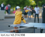 Moscow, Russia - June 4, 2021: Sports activity in the public park. Boy plays table tennis, healthy lifestyle theme. Leisure concept. Ping-pong game in hot sunny day. Редакционное фото, фотограф YuryKara / Фотобанк Лори