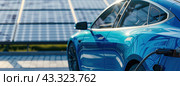 A blue electric car is charging in front of the solar panels. Energy of the future. Стоковое AI-изображение, AI-художник Ярославский Максим / Фотобанк Лори