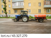 A utility tractor pours water on the road and sidewalk on a hot day. Russia. Moscow. 10.06.24 (2024 год). Редакционное фото, фотограф Ярославский Максим / Фотобанк Лори