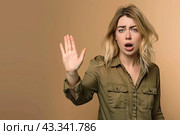 A young lady in a green shirt puts her hand in front of her in fright, asks her to stop and looks at the camera. Стоковое AI-изображение, AI-художник Ярославский Максим / Фотобанк Лори