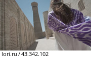 A young woman with long hair in an oriental robe and a skullcap walks through an ancient oriental city. Стоковое видео, видеограф Aleksey Kidisyuk / Фотобанк Лори