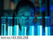 Scientist analyzing test tubes with glowing liquid in a dark lab. Стоковое AI-изображение, AI-художник Антон Гвоздиков / Фотобанк Лори