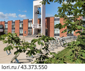 Главный вход в Московский институт электронной техники (МИЭТ). Над ступенями символ в виде электрона. Лист каштана. Стоянка велосипедов. Голубое небо, белые облака. (2024 год). Редакционное фото, фотограф Сергей Никифоров-Гордеев / Фотобанк Лори