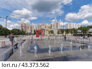 Девушка с собакой  породы такса прогуливается около фонтана на Центральной площади Зеленограда. На фоне новые жилые дома и здание фитнес-центра. Голубое небо, белые облака (2024 год). Редакционное фото, фотограф Сергей Никифоров-Гордеев / Фотобанк Лори