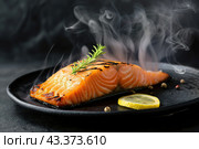 Hot smoked salmon fillet on black plate. Hot lox piece with steamed smoke. Dark background. Salmon steak served lemon, herbs cooking grill barbecue. Grilled red fish dish. Frying trout. Menu, recipe. Стоковое AI-изображение, AI-художник Марина Демидюк / Фотобанк Лори