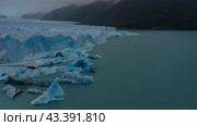 A wall of blue cracked ice rises in a glacial lake. Thawed ice floes, icebergs float in turquoise water. Coastal mountains in clouds and fog. Perito Moreno glacier. Lago Argentino. El Calafate. Стоковое фото, фотограф Вера Ивановна Кубарева / Фотобанк Лори