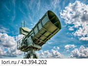 Modern air defence radar of military mobile missile launcher system of green color at blue cloudy sky background. Air defense installation outdoors. Concept of modern army industry. Copy ad text space. Стоковое AI-изображение, AI-художник Aleksandr Golubev / Фотобанк Лори