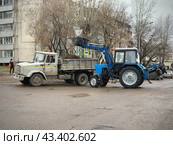 Уборочная техника трактор-экскаватор грузит мусор (прошлогоднюю листву) в грузовик на субботнике (2024 год). Редакционное фото, фотограф Ирина Тульская / Фотобанк Лори
