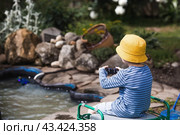 A 5-year-old boy in a yellow panama hat launches a radio-controlled boat in a pond. Children's fun and street games. Child's leisure time. Стоковое фото, фотограф Photojuli / Фотобанк Лори