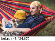 Summer holidays for children in the fresh air. A cute little boy with his father is having fun on a hammock in the backyard. A child and a dad in a hammock. Стоковое фото, фотограф Photojuli / Фотобанк Лори