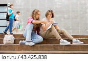 Girl prompts solution to problem to young man sitting on stone staircase in front of school. Стоковое фото, фотограф Яков Филимонов / Фотобанк Лори
