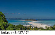Beautiful postcard view. A sandbar meanders towards a tropical island with green vegetation. Tiny silhouettes of people on the beach. Boats in the aquamarine ocean. Palm leaves in the foreground. Стоковое фото, фотограф Вера Ивановна Кубарева / Фотобанк Лори