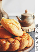 Different types of bread - kalacha, hala - braided loaf with coarse salt. Bread on table with kettle and jug, prepared for consumption. Assortment of handmade bread. Стоковое фото, фотограф Оксана Медведева / Фотобанк Лори