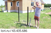 Chain-link fence is built on garden plot in nature, landowner twists ends wire of chainlink fence together. Стоковое видео, видеограф Владимир Григорьев / Фотобанк Лори