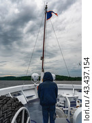 Deck of a ship, lake view, north sea from aboard a cruise ship. Unrecognizable silhouette of a man in a hood. Lone man on deck. Theme of traveling in northern regions and cold water spaces. Стоковое фото, фотограф Оксана Медведева / Фотобанк Лори