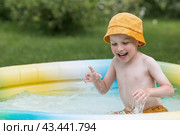 It's a hot day. A cute boy is swimming and splashing in the pool. A happy little boy smiles at the camera. Splashes of water are flying in all directions. The concept of summer holidays with children. Стоковое фото, фотограф Photojuli / Фотобанк Лори