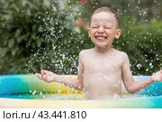 It's a hot day. A cute boy is swimming and splashing in the pool. A happy little boy smiles at the camera. Splashes of water are flying in all directions. The concept of summer holidays with children. Стоковое фото, фотограф Photojuli / Фотобанк Лори