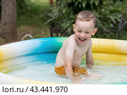 It's a hot day. A cute boy is swimming and splashing in the pool. A happy little boy smiles at the camera. Splashes of water are flying in all directions. The concept of summer holidays with children. Стоковое фото, фотограф Photojuli / Фотобанк Лори