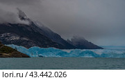 A wall of blue ice crosses a turquoise glacial lake. The glacier stretches to the horizon between the mountains. Cloudy, foggy. Perito Moreno. El Calafate. Lago Argentino. Argentina. Стоковое фото, фотограф Вера Ивановна Кубарева / Фотобанк Лори