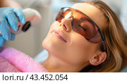 During the laser treatment, a woman is having her face worked on by a professional. Стоковое AI-изображение, AI-художник Юрий Поздников / Фотобанк Лори