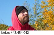 Satisfied Traveler Guy Wearing Red Hoody Stands in Picturesque Place of Wildlife, Looks Up at Autumn Landscape. Concept People Traveling and Success. Low Angle Shot of 30s Man in Fall Nature Closeup. Стоковое видео, видеограф Марина Демидюк / Фотобанк Лори