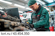 A man wearing a green uniform is working on repairing a car engine inside a garage. Стоковое AI-изображение, AI-художник Юрий Поздников / Фотобанк Лори