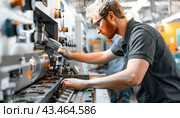 In a factory environment, a man is concentrating on using a machine for his job. Стоковое AI-изображение, AI-художник Юрий Поздников / Фотобанк Лори