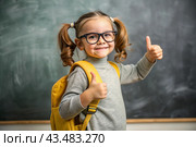 A cute girl with glasses shows the class with her hand. The child goes to school for the first time. A child with a school bag and a book. A child in the classroom on the background of a blackboard. Back to school. Стоковое AI-изображение, AI-художник Photojuli / Фотобанк Лори